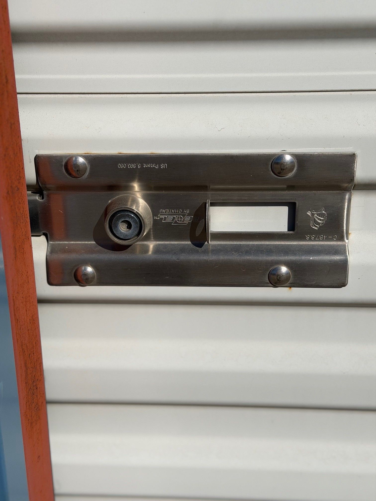 Silver metal storage unit lock, with keyhole and bolt, attached to a white rolling door.