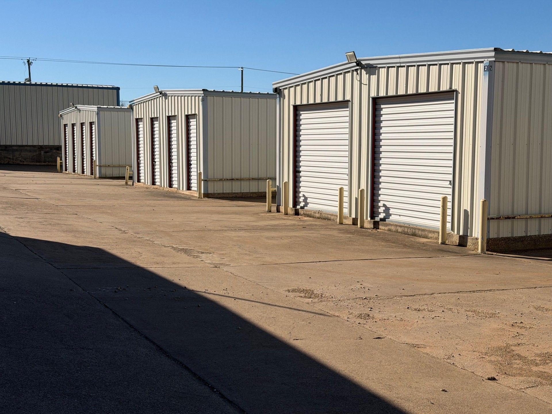 Row of off-white storage units with roll-up doors, outdoors on a sunny day.