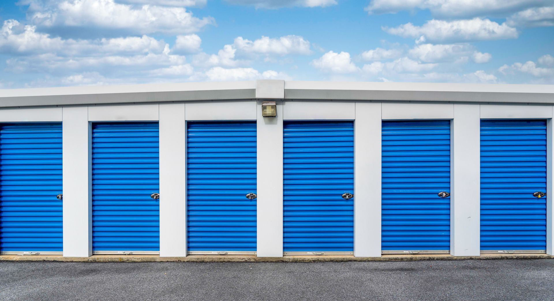 Row of storage units with bright blue roll-up doors at an outdoor self-storage facility.