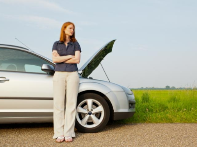 Woman standing beside silver car with open hood, looking frustrated, outdoors.