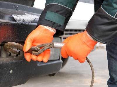 Person in orange gloves attaching a tow cable to the bumper of a black car.