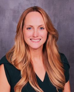 Smiling woman with long blonde hair in a dark green top against a gray backdrop