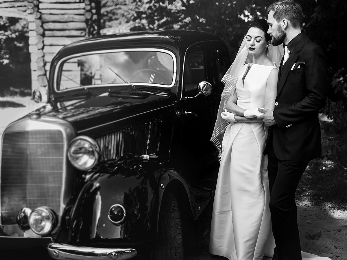 A bride and groom are posing for a picture in front of an old car.