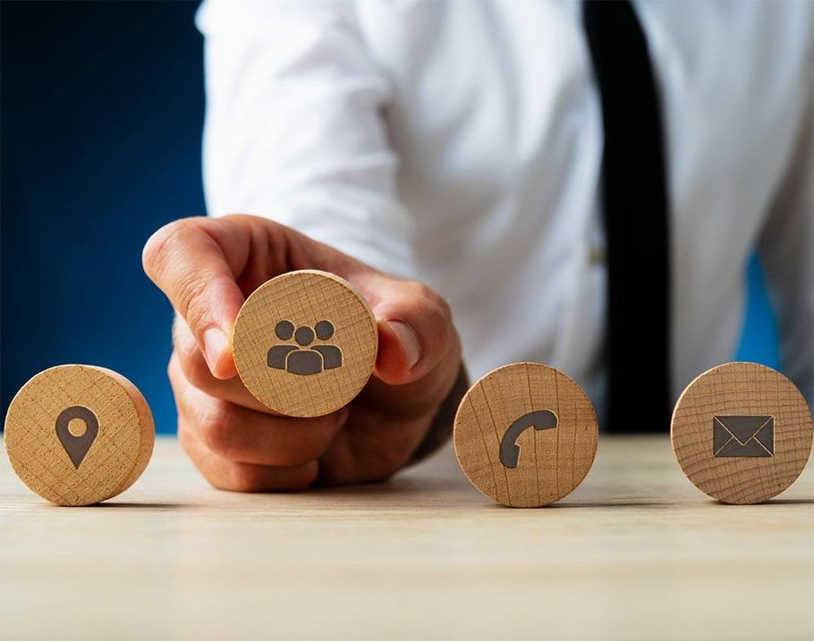 A person is holding a wooden block with a contact icon on it.