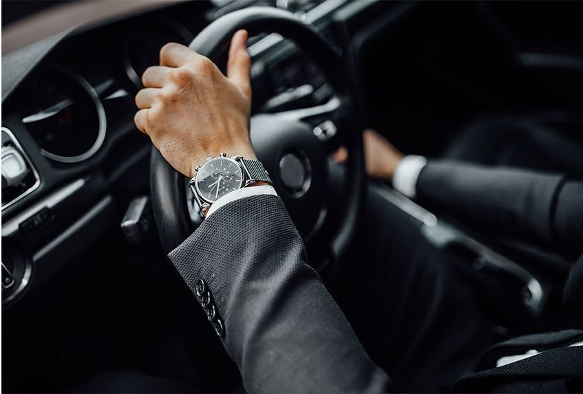 A man in a suit is driving a car and wearing a watch.