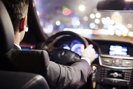 A man in a suit is driving a car at night.