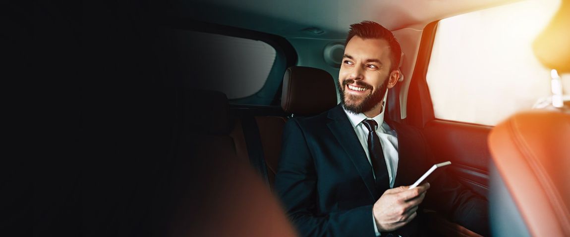 A man in a suit and tie is sitting in the back seat of a car holding a cell phone.