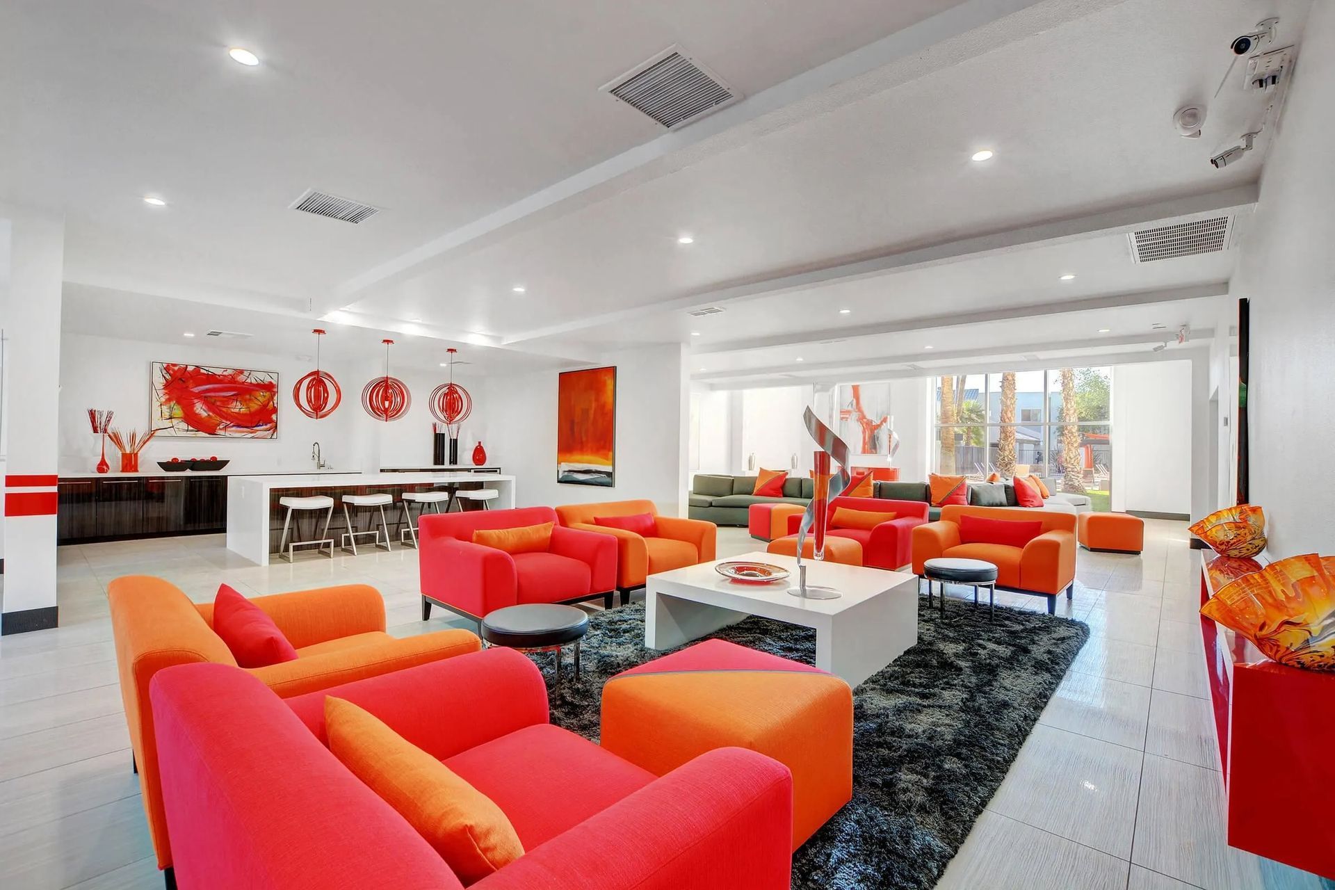 Bright modern lounge with red and orange sofas, black rug, wall art, and large windows