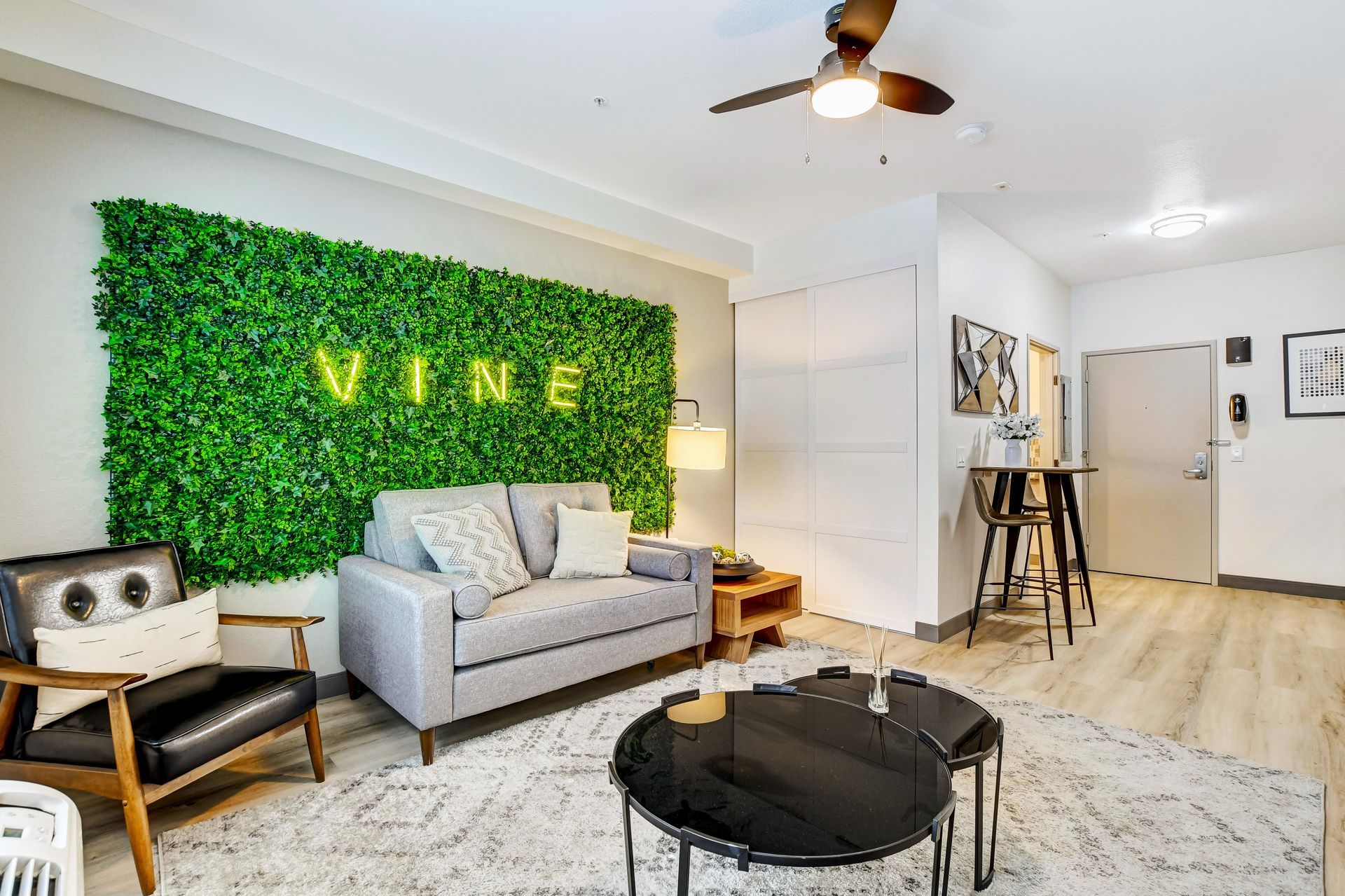 Modern living room with green plant wall, gray sofa, black chairs, and light wood floor