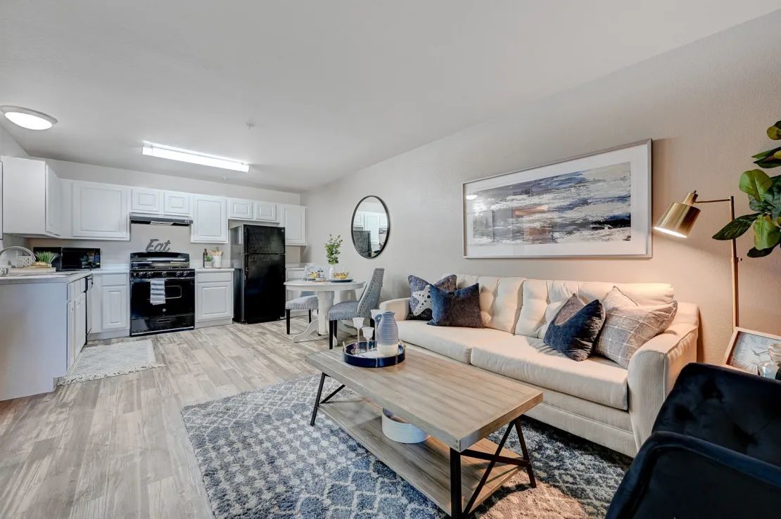 Bright modern living room with beige sofa, coffee table, patterned rug, and open kitchen in the background