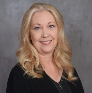 Headshot of a smiling woman with long blonde hair, wearing a black top against a gray backdrop