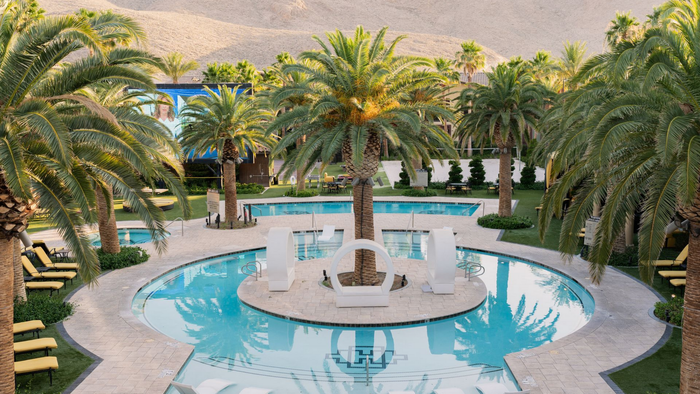 Palm-lined resort pool with a circular fountain and white loungers at sunset