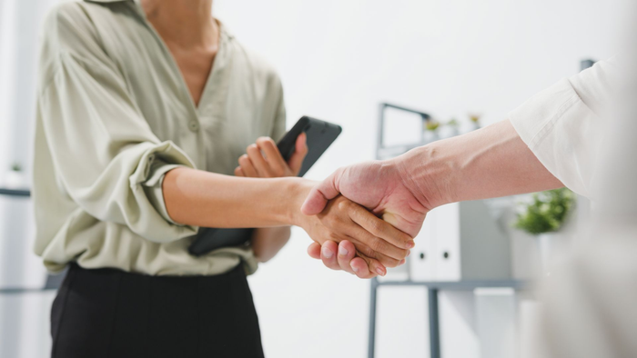 Two people shaking hands in an office, with one person holding a tablet.