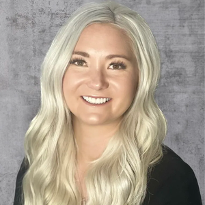Smiling person with long platinum-blonde hair against a gray textured backdrop
