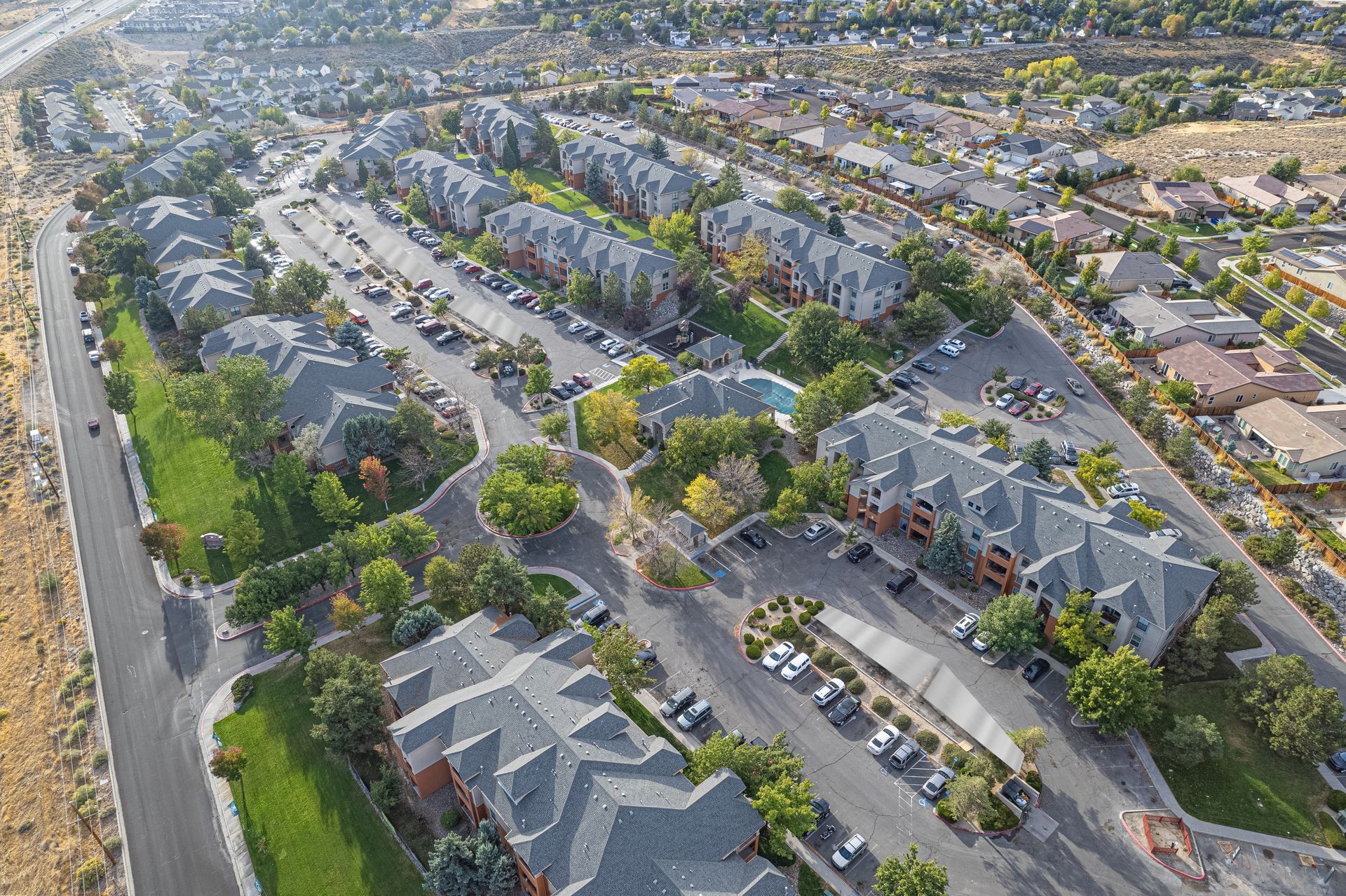 Aerial view of a suburban apartment complex with parking lots, tree-lined streets, and rows of townhomes.