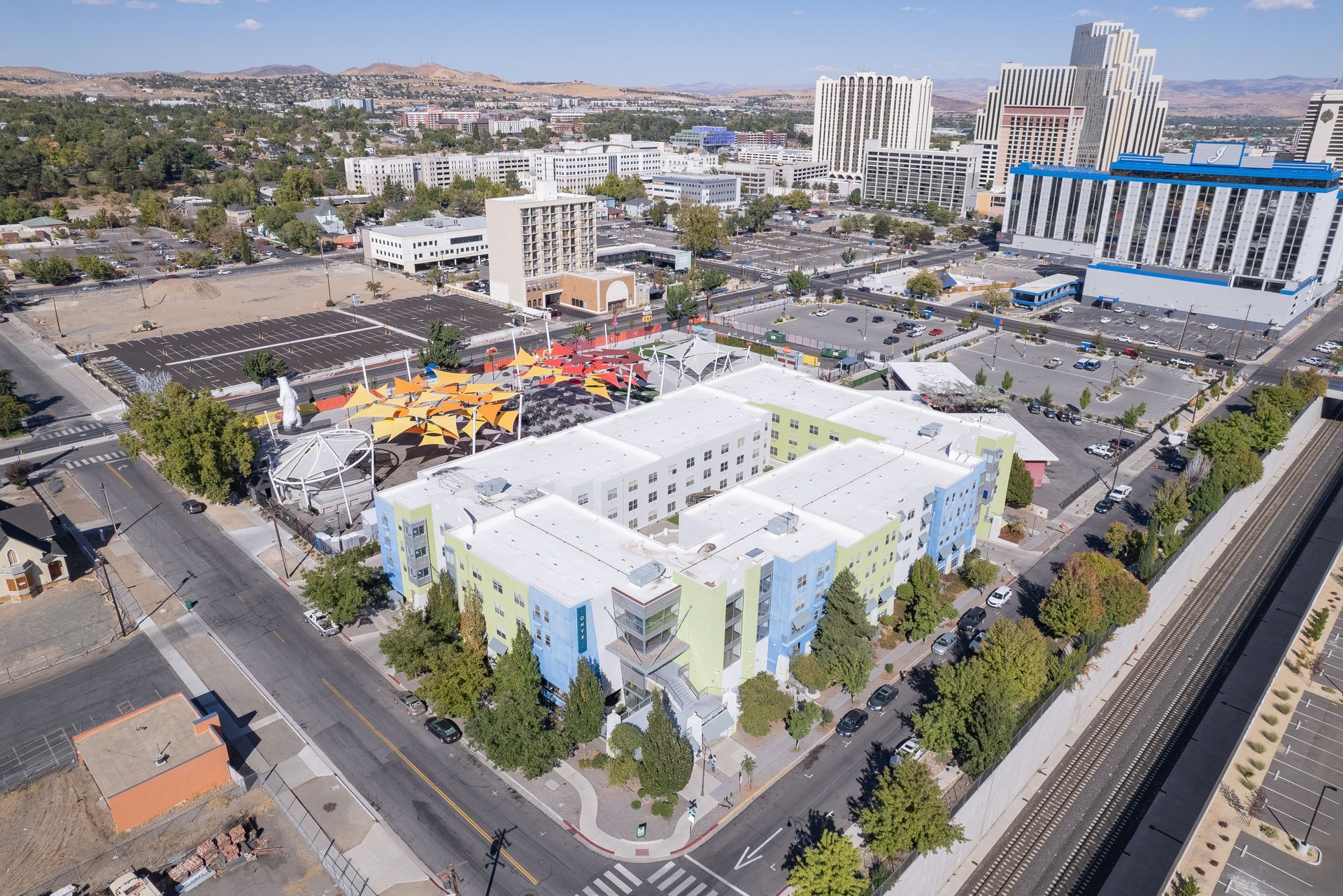 Aerial view of a modern white building complex with a colorful courtyard and nearby roads in a city area