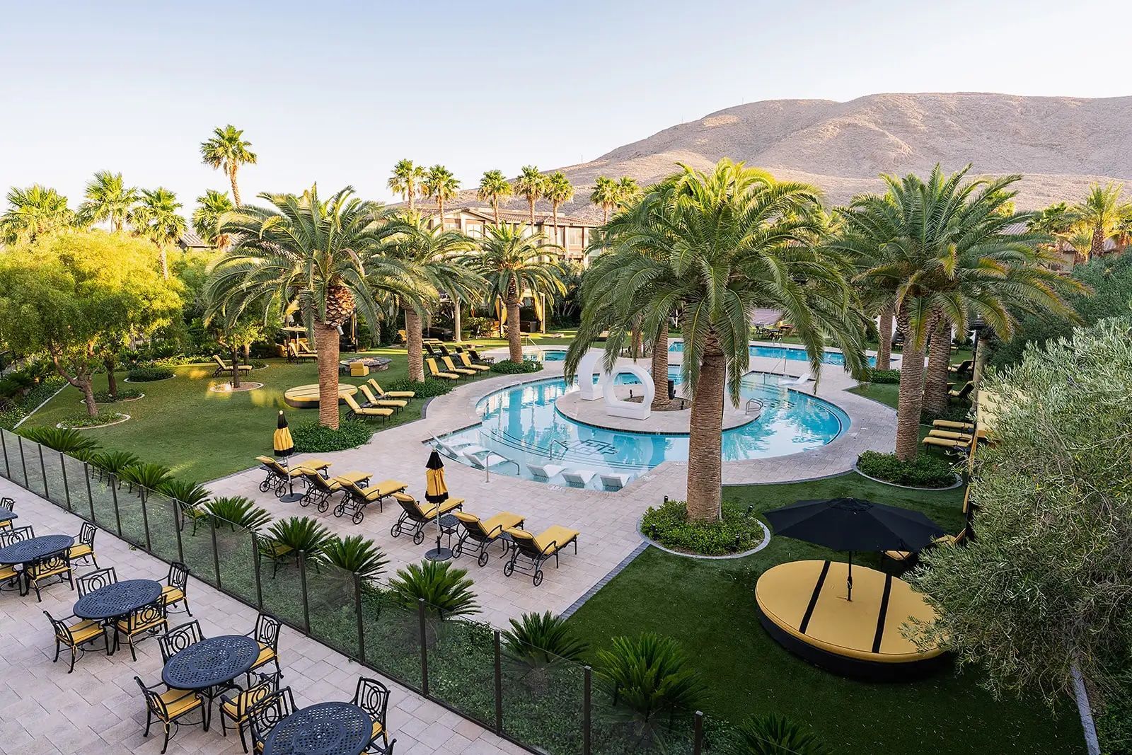 Resort pool with palm trees, lounge chairs, and mountain backdrop in warm evening light
