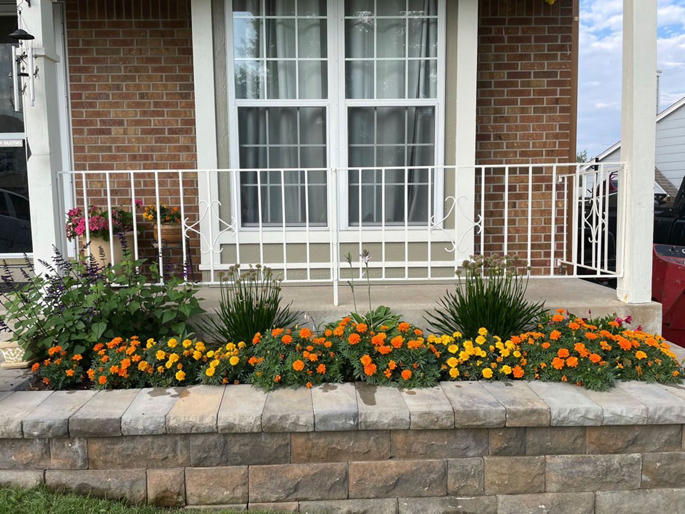 A brick house with a white railing and flowers in front of it.