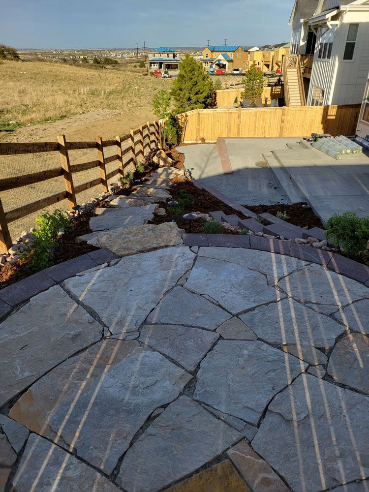 A stone patio with a wooden fence in the background and a house in the background.