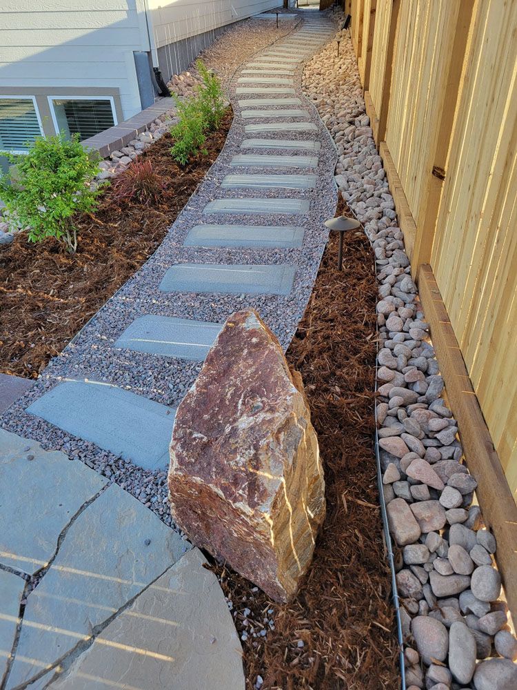 A stone walkway next to a wooden fence with a large rock in the middle.