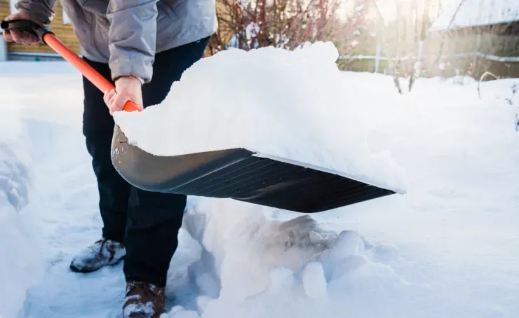 A person is shoveling snow from a sidewalk with a shovel.