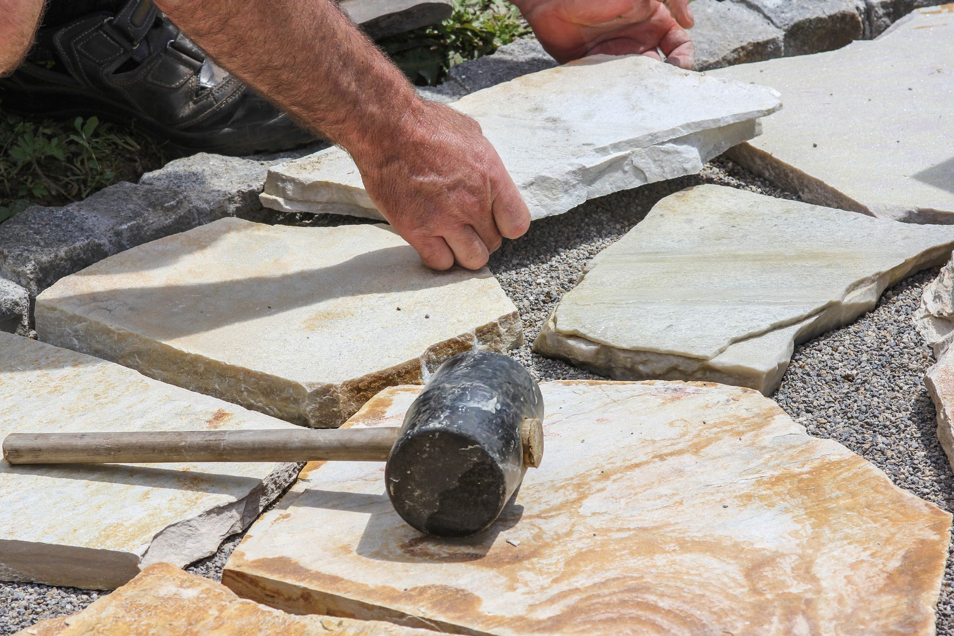 A man is laying a stone walkway with a hammer.