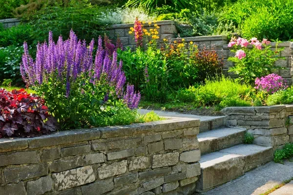 A stone wall surrounds a garden filled with lots of flowers and plants.