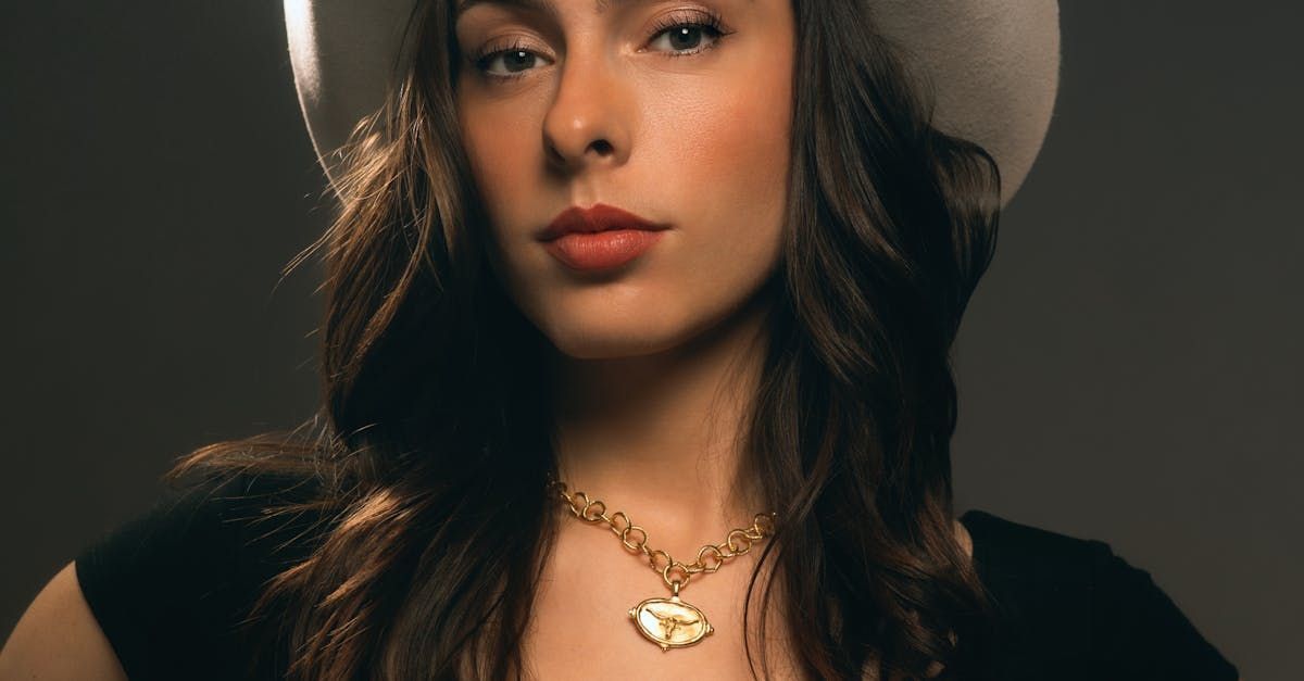 A woman wearing a hat and a necklace is looking at the camera.