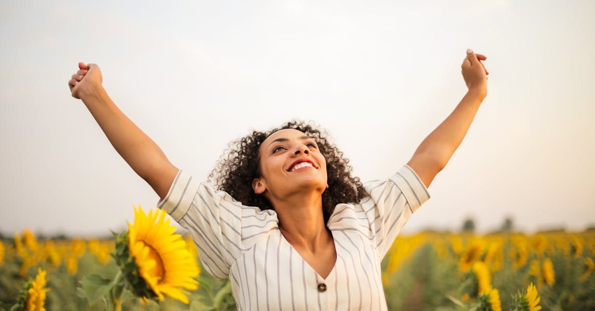 A woman is standing in a field of sunflowers with her arms outstretched.