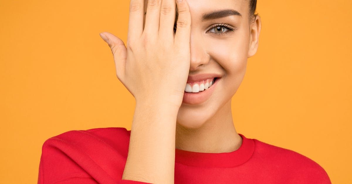 A woman is smiling and covering her eye with her hand.