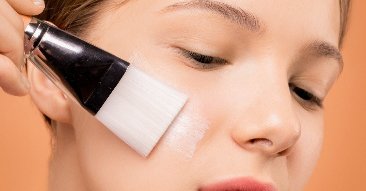 A woman is applying a mask of retinol to her face with a brush.