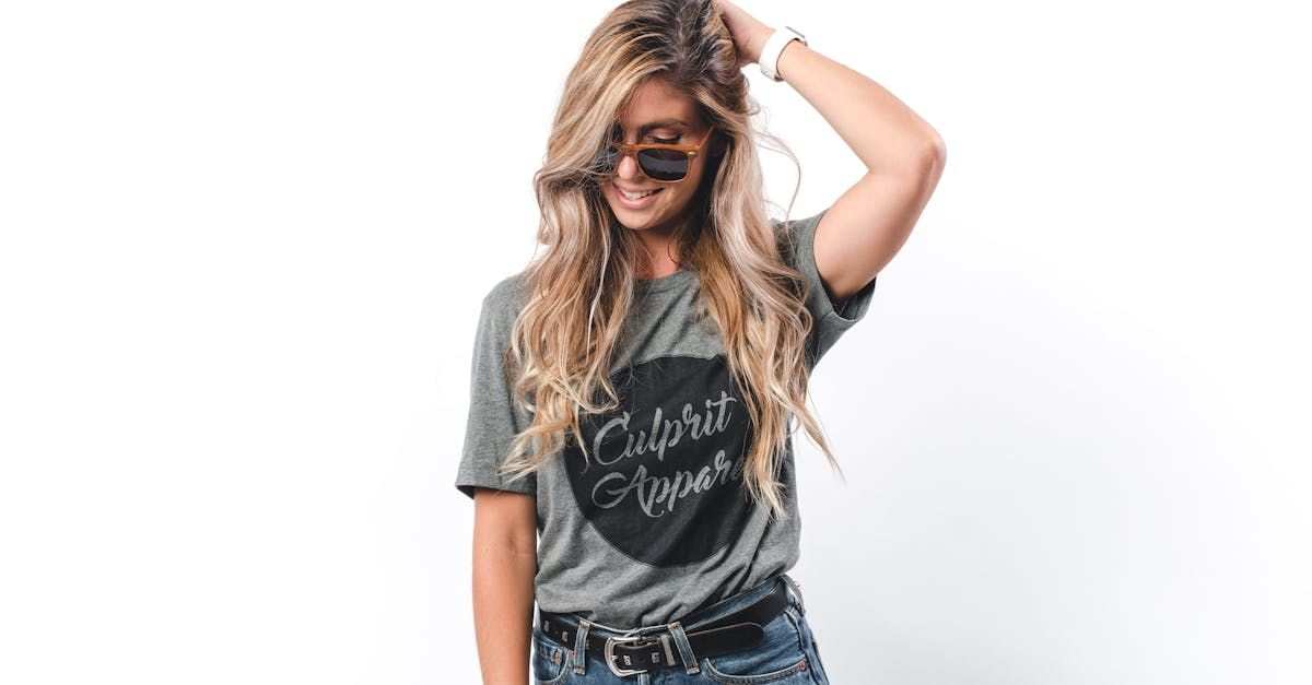 A woman wearing a t-shirt and sunglasses is standing in front of a white background.