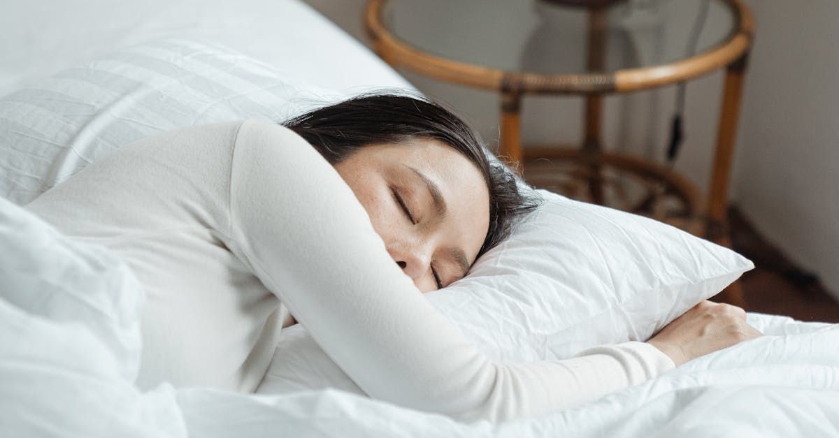 A woman is sleeping on a bed with white sheets and a pillow.