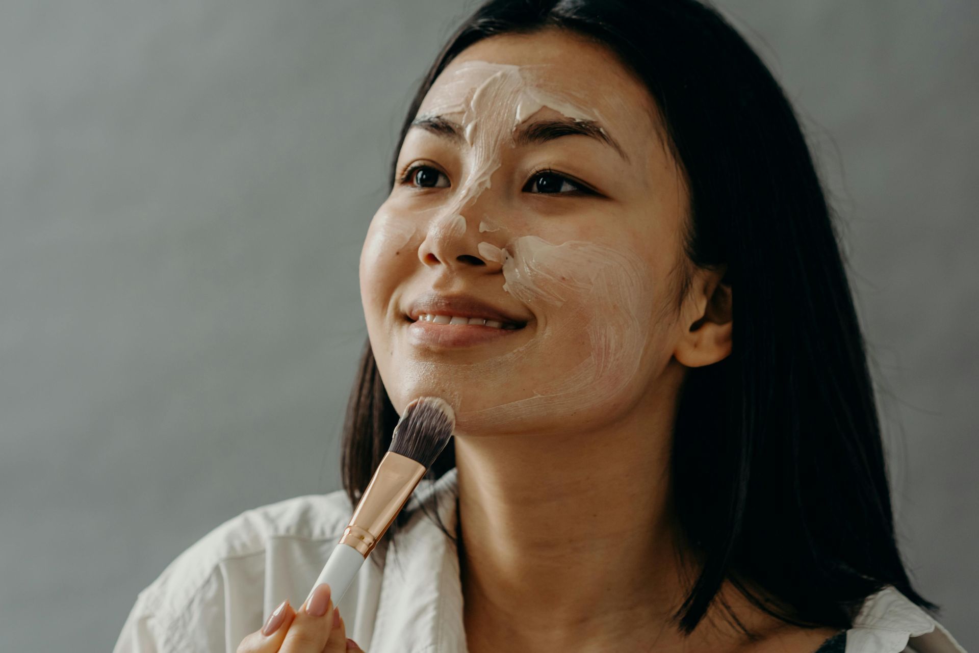 A woman is applying a mask to her face with a brush.