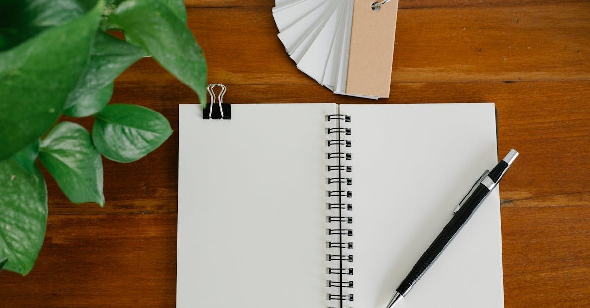 A spiral notebook with a pen and a fan on a wooden table.