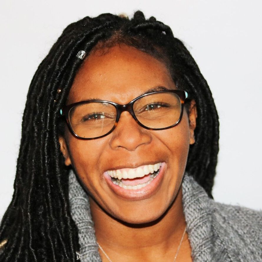 a woman wearing glasses and a grey sweater is smiling
