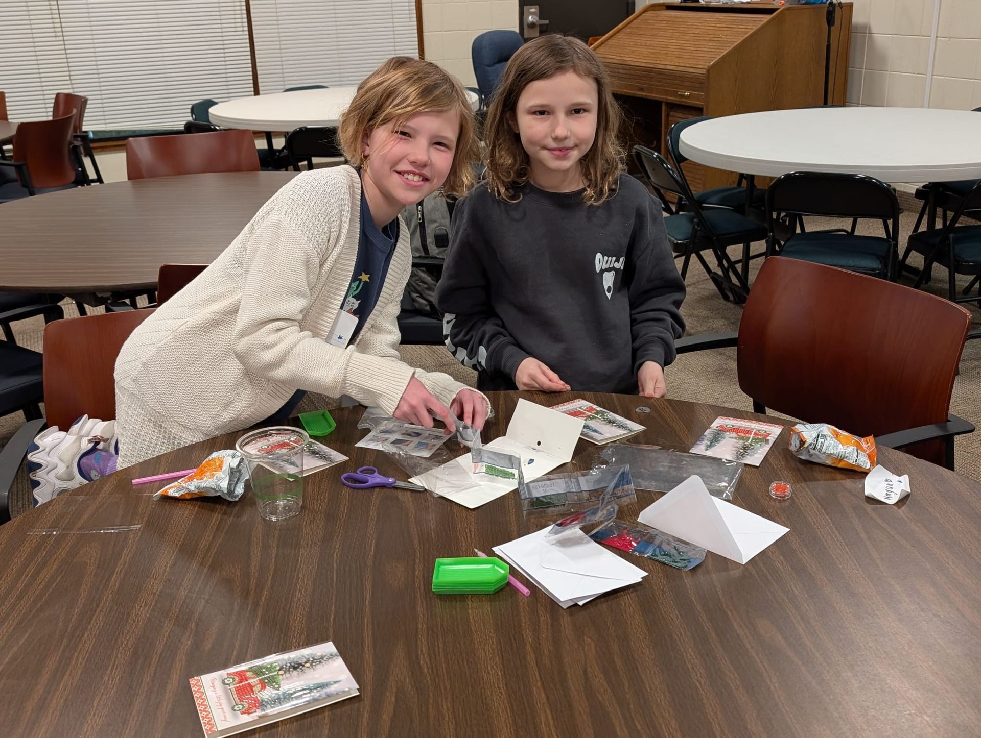 Two young girls are sitting at a table making crafts.