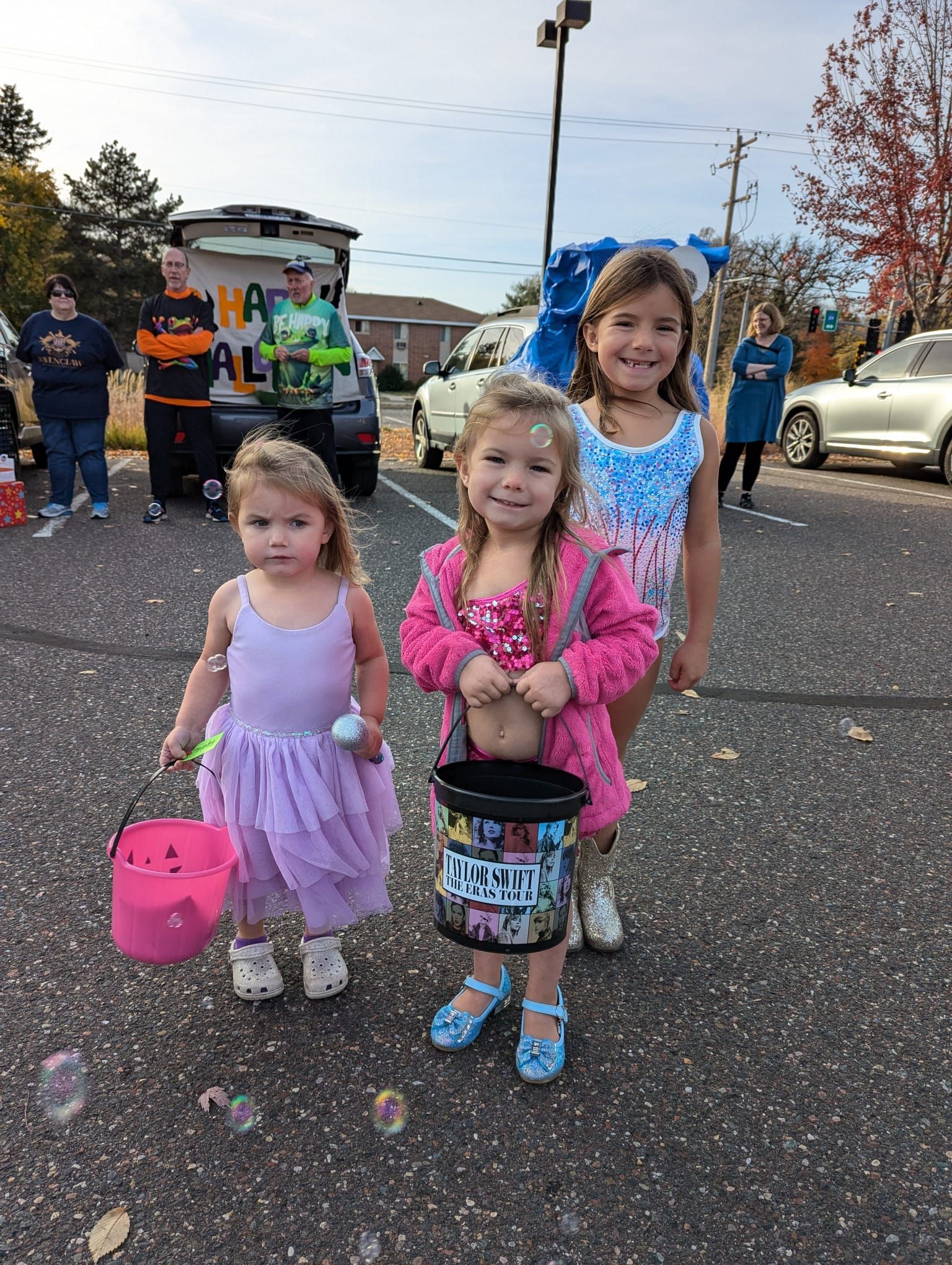 Three little girls are standing next to each other in a parking lot.