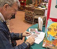 A man is sitting at a table signing a book.