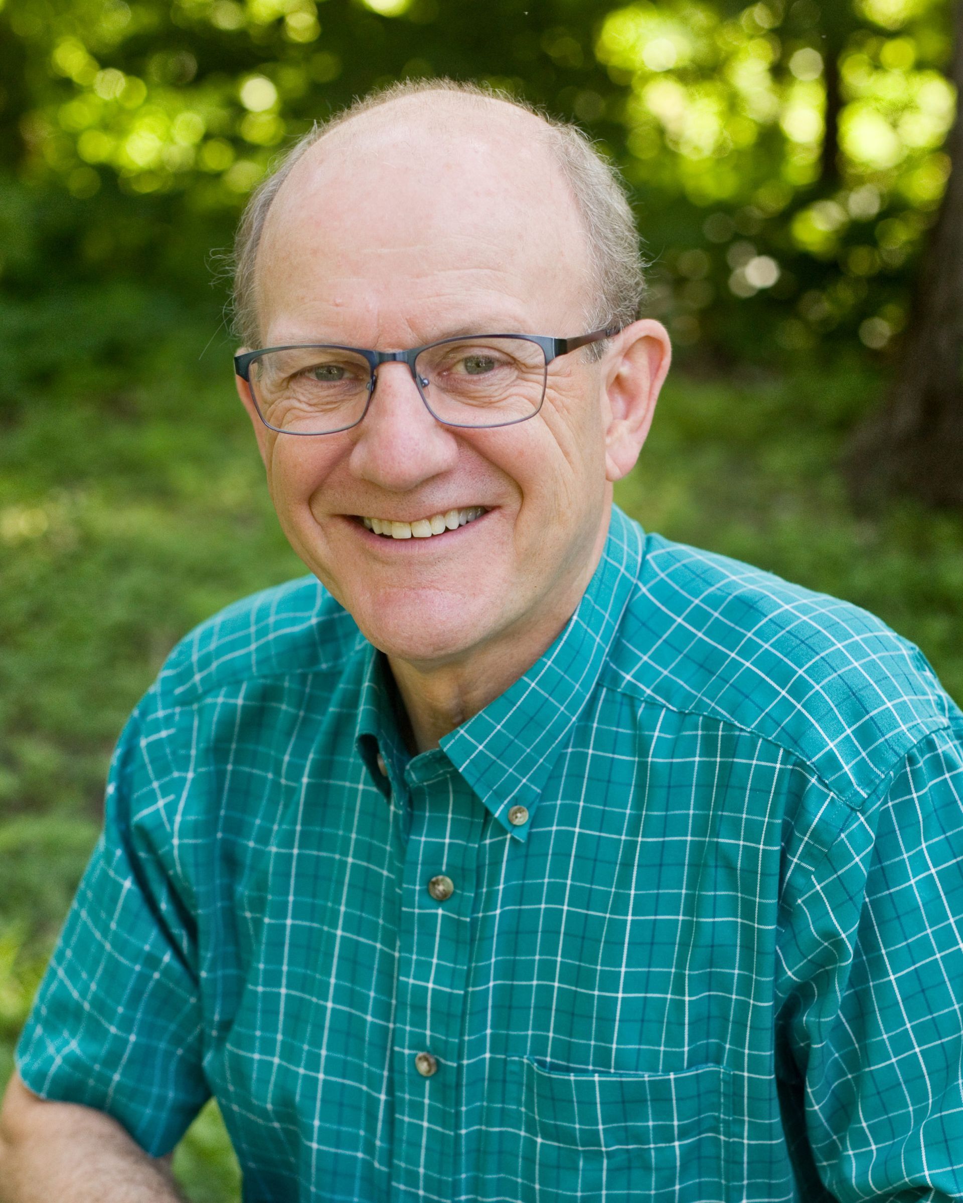 A man wearing glasses and a green shirt is smiling for the camera.
