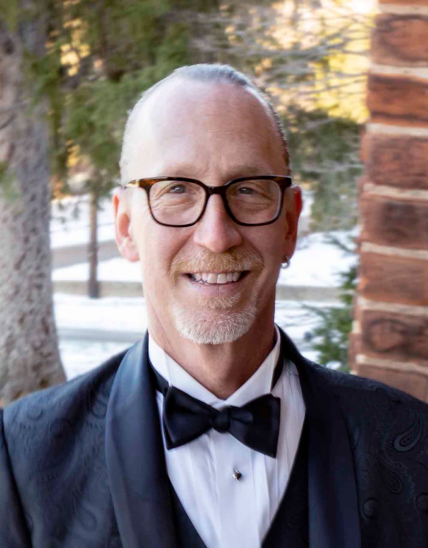 A man in a tuxedo and bow tie is smiling for the camera.