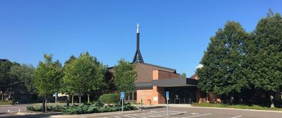 A church with a cross on top of it is surrounded by trees and a parking lot.