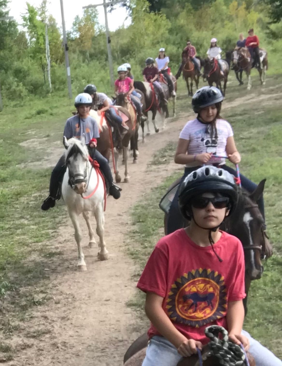 A group of people are riding horses down a dirt path