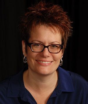 A woman wearing glasses and earrings is smiling for the camera.