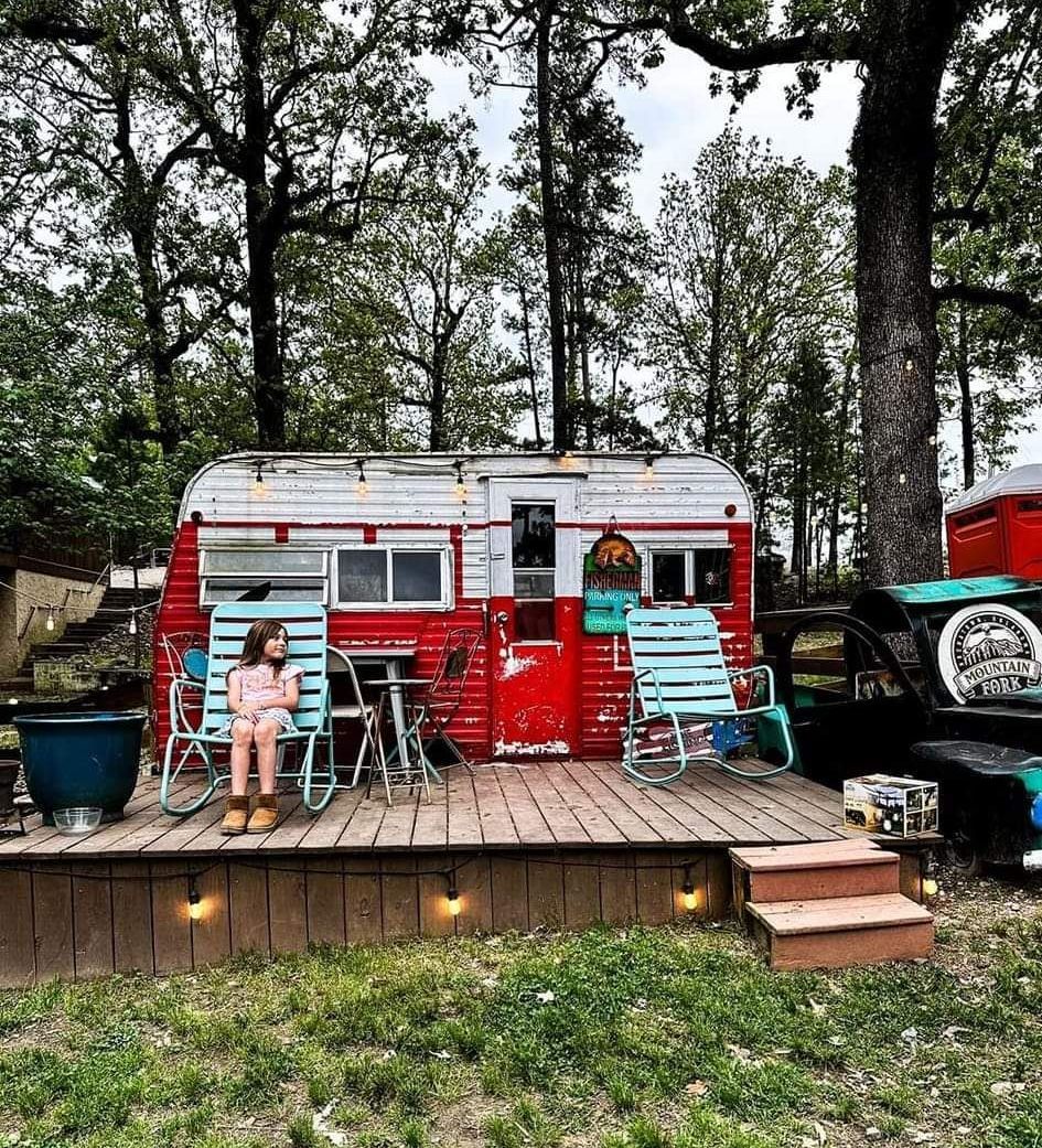 A girl is sitting on a deck in front of a red trailer.