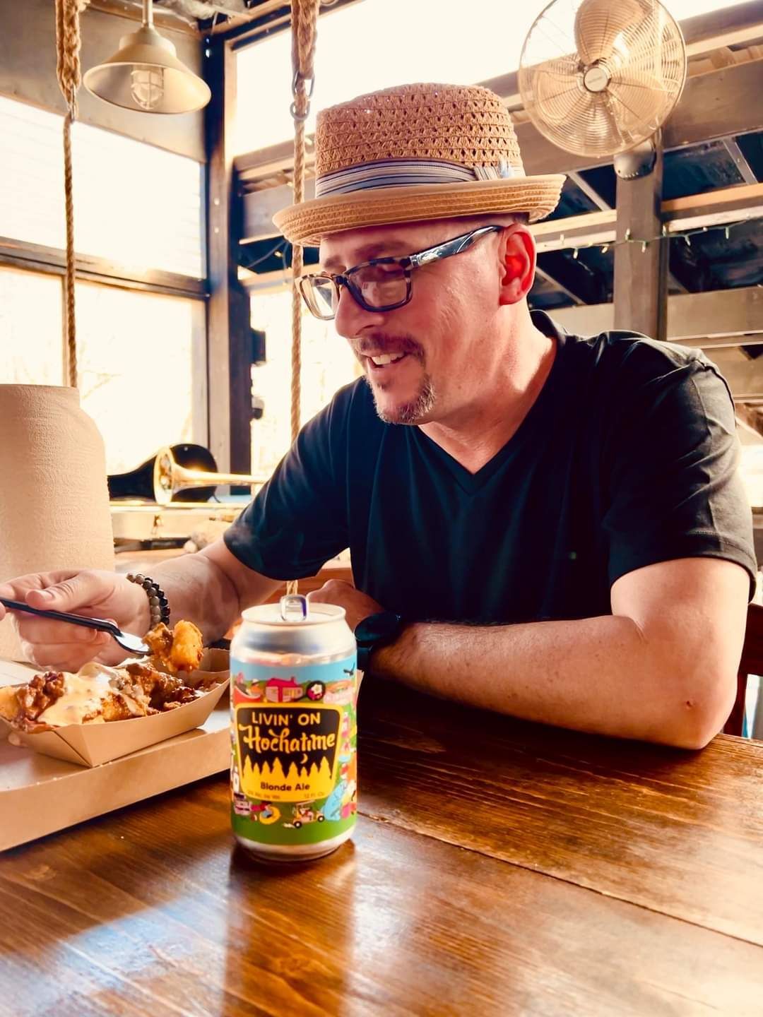 A man in a straw hat is sitting at a table with a can of beer.