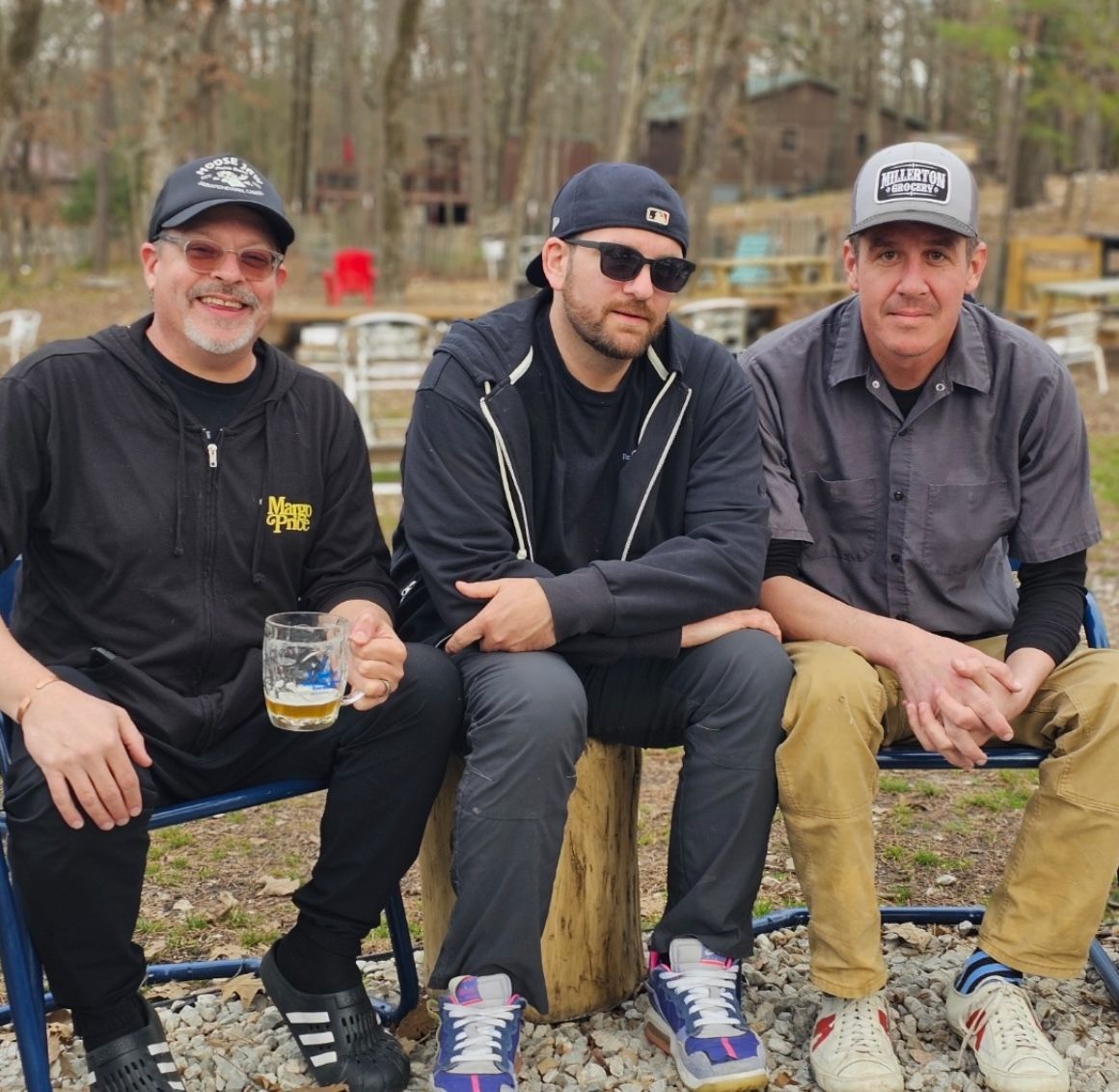Three men are sitting on a bench with one holding a glass of beer