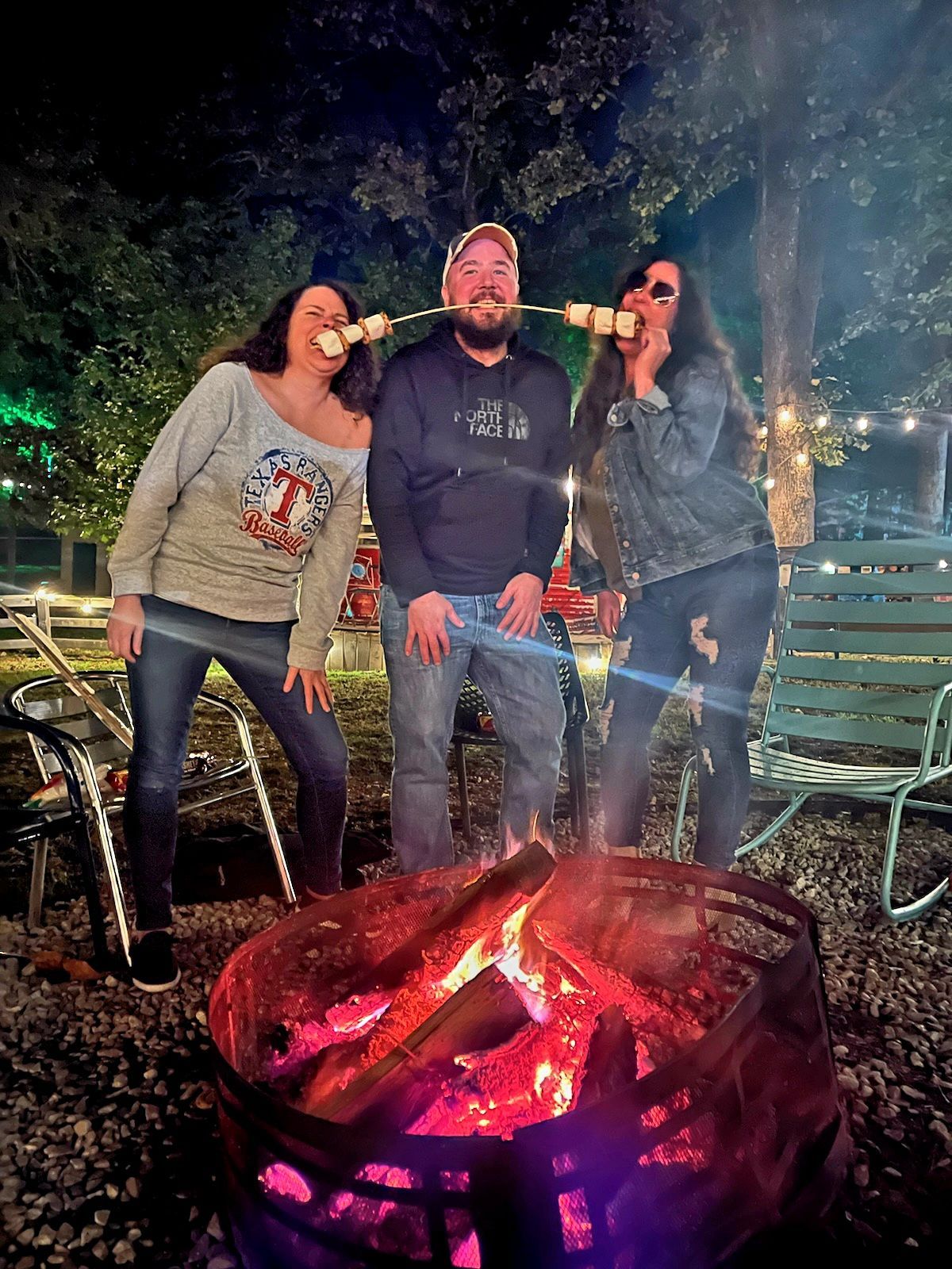A group of people are standing around a fire pit eating marshmallows.