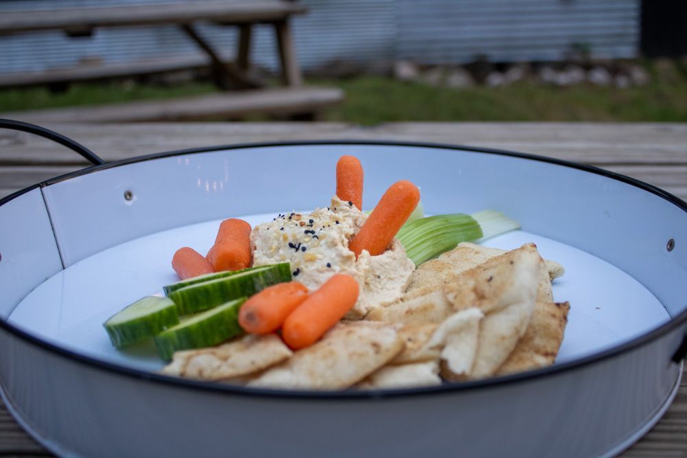A white plate topped with carrots , cucumbers , and pita chips on a wooden table.