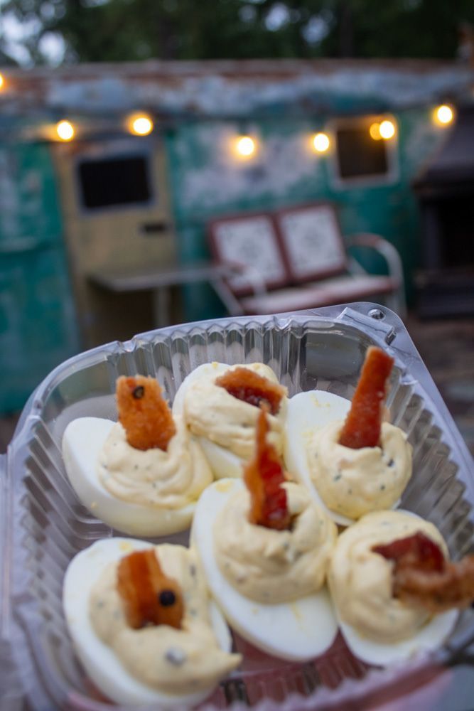 A plastic container filled with stuffed eggs and bacon.